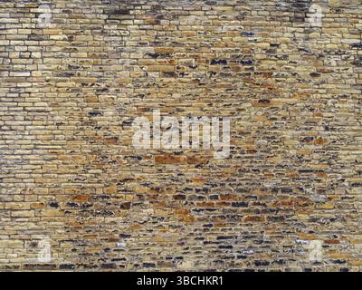 Brown and yellow outdoor stone wall with many uneven rough bricks and textured surface Stock Photo