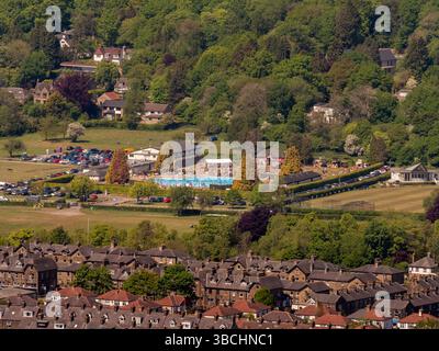 A distant view of Ilkley Lido, nestled among trees and surrounded by houses and green fields, seen from Ilkley Moor, Yorkshire. UK Stock Photo