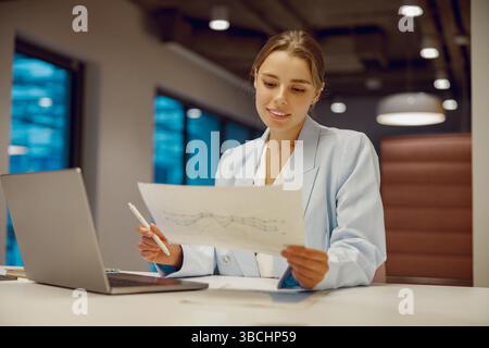 A professional businesswoman carefully analyzing the latest market trends in a modern office space Stock Photo