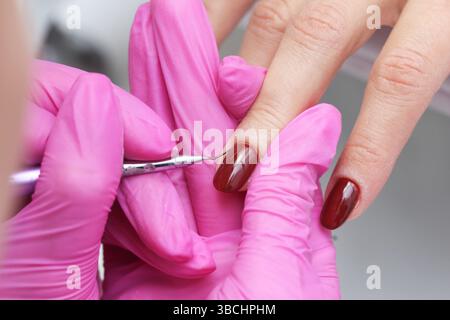 Manicurist painting nails. Closeup of hand care. Beauty treatment process. Red gel polish manicure. Professional nail stylist at work. Female fingers. Stock Photo