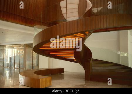 The elegant modern architectural grand spiral wood staircase with warm under-step lighting and a glass railing Stock Photo