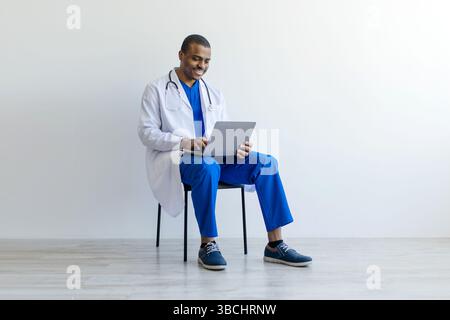 African American male doctor sitting on chair and using laptop, Stock Photo