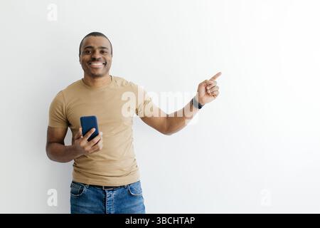 Smiling Black Man Holding Smartphone And Pointing Aside At Copy Space Stock Photo