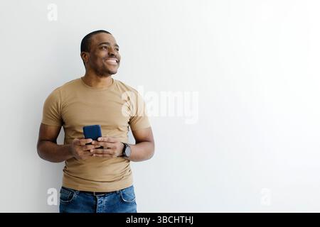 African American man holding smartphone with both hands and looking aside Stock Photo