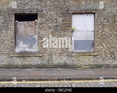 Front view of an old abandoned derelict house on an empty street with boarded up windows and dilapidated brick walls Stock Photo