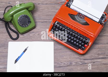 The photo shows a typewriter, telephone and a notebook on a wooden table Stock Photo