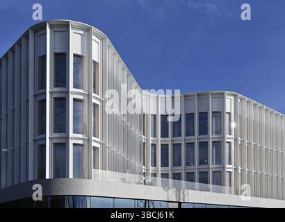 The image showcases a modern architectural building with a sleek and wavy facade. The structure features large, vertically aligned windows framed by Stock Photo