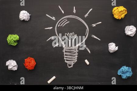 Crumpled paper on a blackboard with a handdrawn lightbulb, new idea concept background Stock Photo