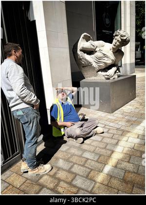 Two workmen in a London street, next to a statue, having a break, one shielding his eyes from the sun. Stock Photo