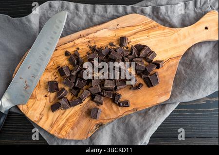 Chopped Bar of Baking Chocolate on Cutting Board: Chopped pieces of unsweetened chocolate on a wooden cutting board with knife Stock Photo
