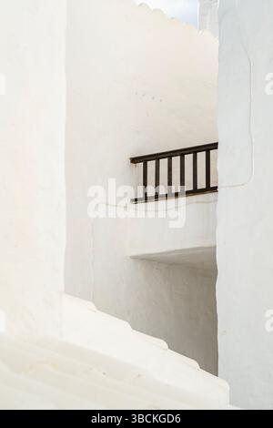 Minimalist white architecture with dark railing in a narrow Mediterranean alleyway. Abstract composition, clean lines, bright sunlight, textured walls Stock Photo