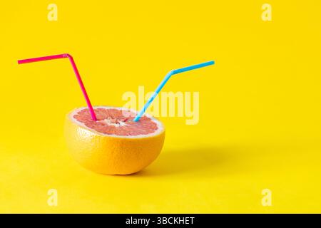 fresh fruit juices. Healthy eating concept. Vitamin-packed grapefruit with drinking straws stuck in it. Yellow background, copy space Stock Photo