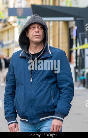 Portrait of a middle-aged man in casual clothes against a city background, a street with blurred passers-by Stock Photo