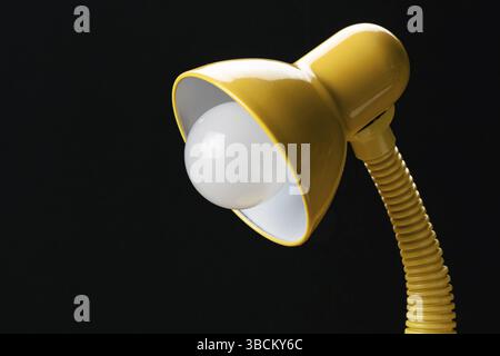 Side view of adjustable yellow desk lamp isolated on black background. Desk lamp with energy saving led light bulb Stock Photo