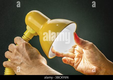 Putting new led light bulb into the socket of desk lamp. Senior hand replaced new light bulb of reading lamp and turning on Stock Photo