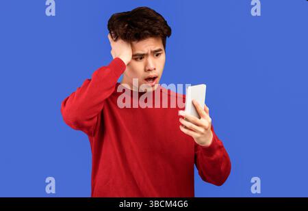 Surprised asian man using mobile phone on blue wall Stock Photo