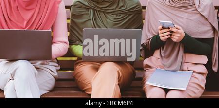 Unrecognizable Arabic Women Using Phone And Laptops Learning Online Outdoors Stock Photo