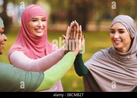 Three Modern Muslim Ladies Giving High-Five Standing In Park Outside Stock Photo