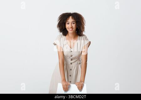 Portrait of cheerful curly african american young woman leaning on chair looking at camera and smiling Stock Photo