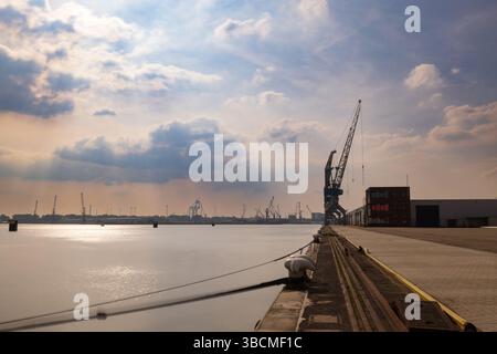 Industrial dock with cranes along the Port of Rotterdam, bathed in warm light under dramatic cloud cover and calm water. Long exposure technique. Stock Photo