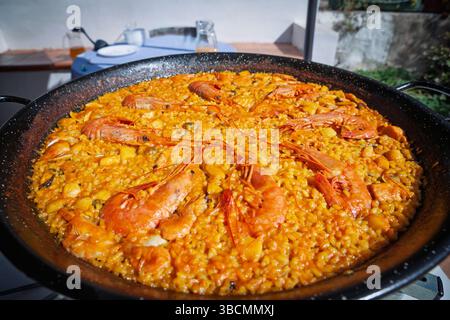 Close-up view of traditional Valencian seafood paella (paella de mariscos) in black pan; saffron rice dotted with mussels and topped with whole prawns Stock Photo
