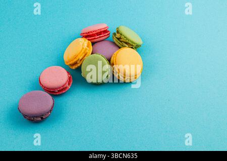 Several vibrant macarons in various colors sit on a smooth, bright blue background, showcasing their delicate textures and unique flavors. Stock Photo