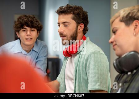 Diverse young coworkers brainstorm around a laptop in a modern workspace, sharing ideas and teamwork on a creative tech project. Stock Photo