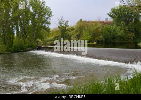 Man-made waterfall (weir) on the Ter River in Roda de Ter, Spain. Water cascades over the structure amidst lush green riverbanks. Catalonia. Stock Photo