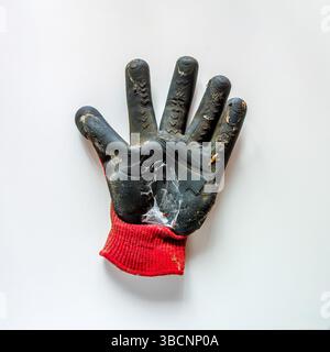 A gardening glove with a black rubber palm and a red knitted cuff is lying flat on a white surface. The glove shows significant wear and dirt Stock Photo