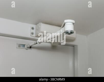 Close-up view of a door closer hinge mounted on a metal white door. Stock Photo
