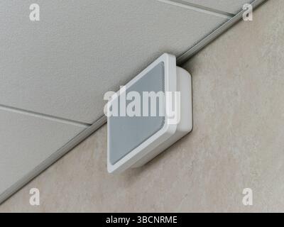Emergency and fire alarm system speaker mounted on the wall under the suspended ceiling. Stock Photo