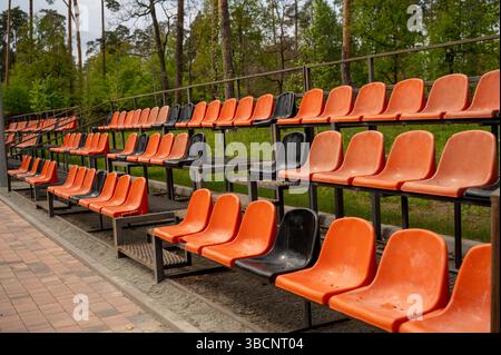 Rows of empty orange and black plastic seats on the grandstand near the outdoor sports stadium Stock Photo