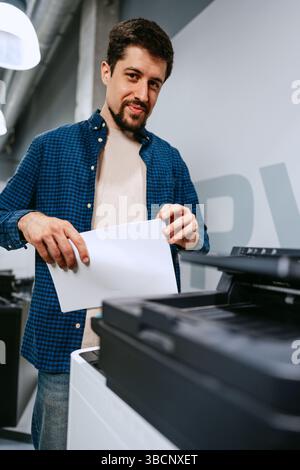 Man operates printer in modern office space while preparing printed documents for work tasks Stock Photo
