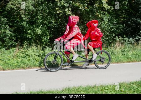 Couple wearing pink elephant costume riding a tandem bike in Munich park, Bavaria, Germany,Europe Stock Photo