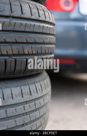 Close-up of stacked tires showing worn and newer tread, with a blurred car in the background, ideal for auto service or maintenance themes. Stock Photo