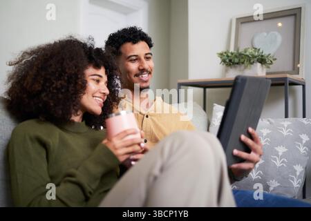 Young Couple Relaxing on a Couch at Home While Using a Tablet Stock Photo