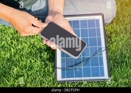 Unrecognizable person using the solar panels power for charging a smartphone at outdoor. Energy concept. Stock Photo