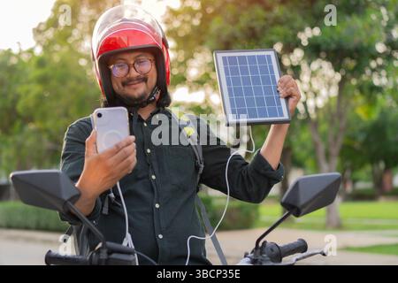 Cropped view of happy man sitting on a motorcycle while carrying solar panel. Integration of solar power as sustainable energy source. Stock Photo