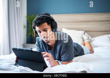 Relaxed Man Using a Tablet With Headphones in a Comfortable Bedroom Setting Stock Photo