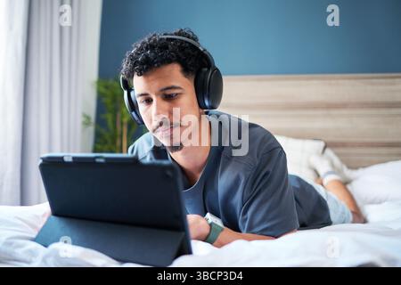 Man Wearing Headphones Relaxing at Home While Using a Tablet in a Comfortable Bedroom Setting Stock Photo