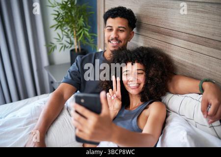 Couple Sitting Together on a Bed Relaxing and Taking a Selfie at Home Stock Photo