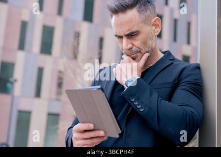 Thoughtful mature man using digital tablet while leaning on pole in city Stock Photo