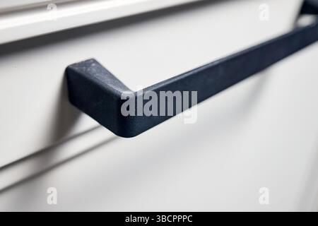 Kitchen cabinet drawer handle closeup. Black metal drawer handle selective focus horizontal shot. Kitchen contemporary interior element. Stock Photo