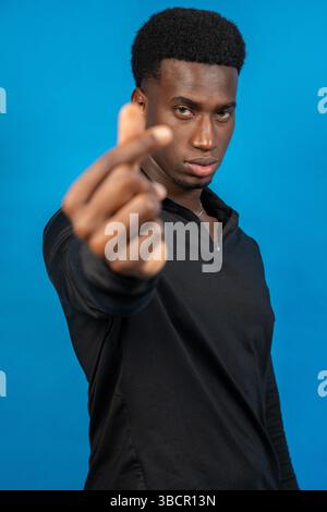 Serious young man pointing his finger on a blue background Stock Photo