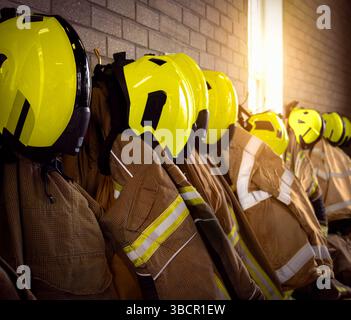 Firefighter firefighting team gear including emergency services helmets, gloves, jacket and trousers with other clothing and equipment in fire station. Stock Photo