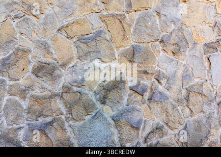 Close-up of a wall made from natural, irregularly shaped beige and gray stones with visible mortar joints. Stock Photo