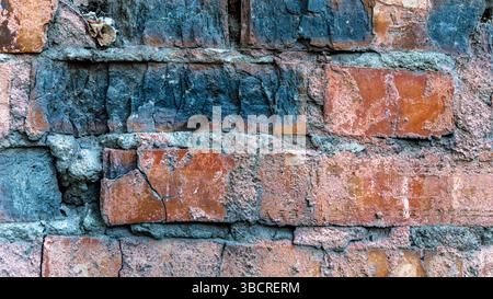 Close-up of an old red brick wall with chipped edges, dark stains, and rough mortar showing signs of aging and decay. Stock Photo