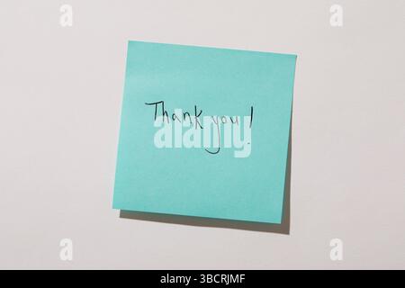 Thank you written on turquoise post it note on wall Stock Photo
