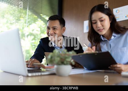 Collaborative Work Environment. Team members smiling while discussing project details on a laptop. Stock Photo
