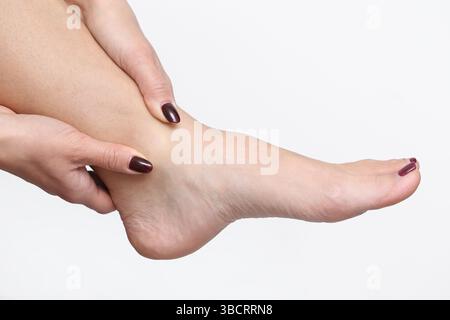 Woman holding sore foot. Pain in ankle area. Female touching leg gently. Medical health issue concept. Injury or fatigue discomfort. Isolated on white Stock Photo